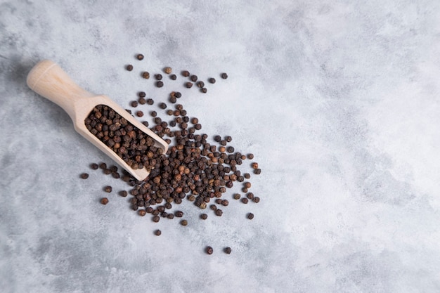 A wooden spoon full of black pepper corns placed on stone table . High quality photo