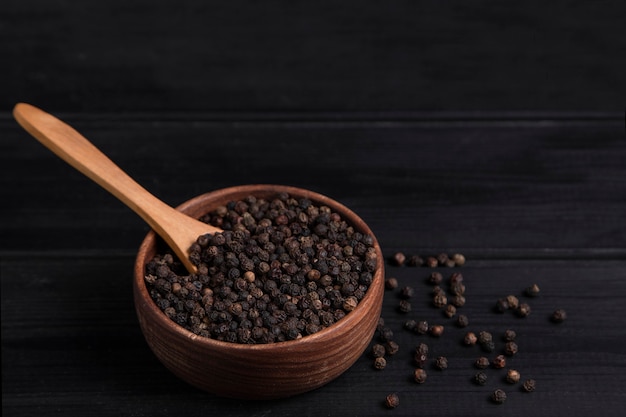 A wooden spoon full of pepper corns placed on a dark wooden table . High quality photo