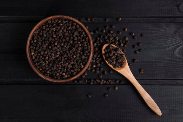 A wooden spoon full of pepper corns placed on a dark wooden table . High quality photo