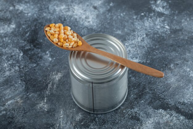 A wooden spoon full of popcorn seeds on marble.
