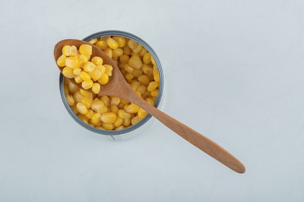 A wooden spoon full of popcorn seeds on white.