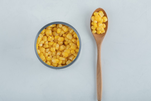 A wooden spoon full of popcorn seeds on white.