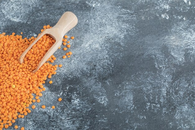 A wooden spoon full of raw lentils on gray.