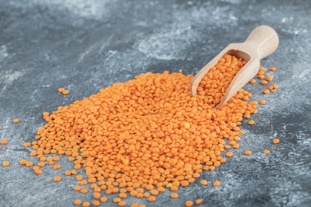 A wooden spoon full of raw lentils on gray.