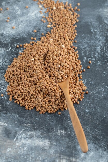 Wooden spoon full of uncooked buckwheat on marble surface