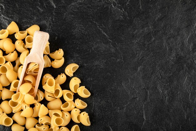 A wooden spoon of uncooked conchiglie macaroni . 