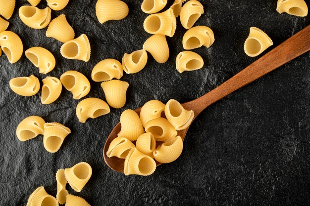 A wooden spoon of uncooked conchiglie macaroni . 