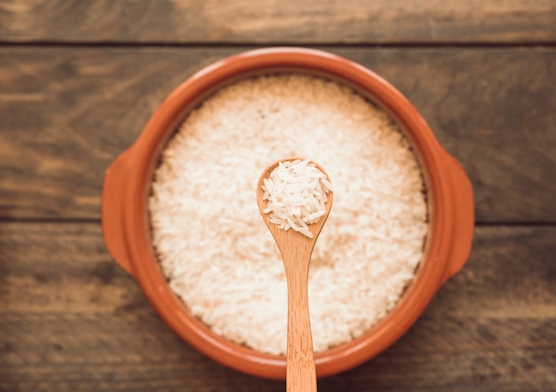 Wooden spoon over the uncooked rice bowl on wooden table