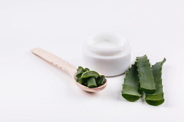 Wooden spoon with aloe lies on a white table with a bottle of white cream