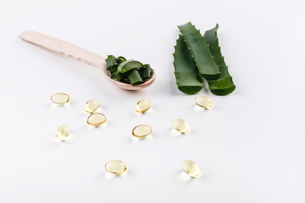 Wooden spoon with aloe lies on a white table with golden capsules with oil