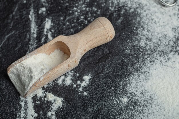 A wooden spoon with flour on black .