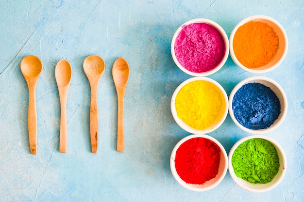 Wooden spoon with holi color powder in the white bowl on painted blue backdrop