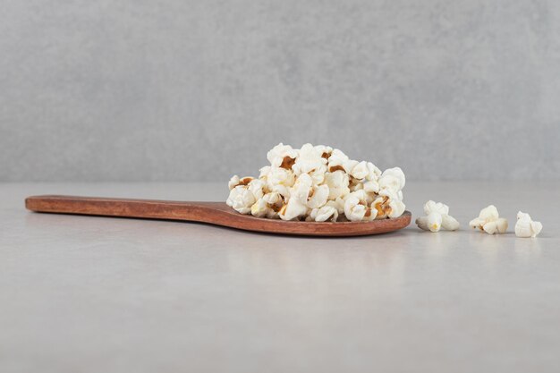Wooden spoon with a small pile of popcorn on top on marble background. 