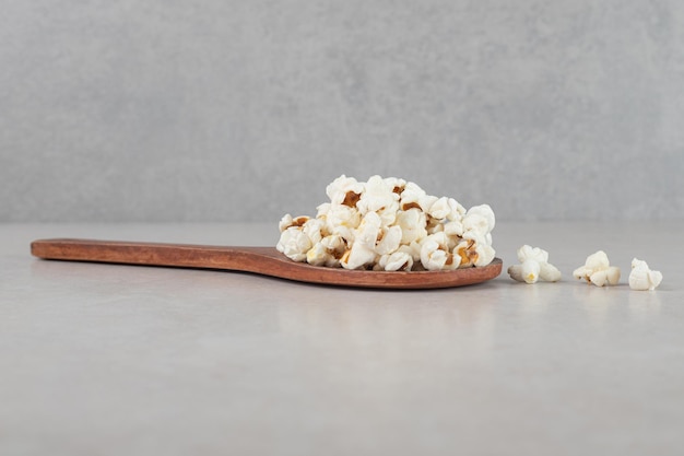 Wooden spoon with a small pile of popcorn on top on marble background. 