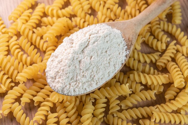 Wooden spoon with wheat flour over raw pasta