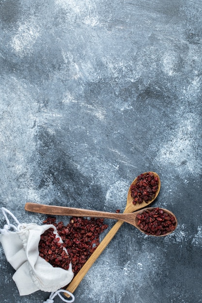 Free photo a wooden spoons full of organic cranberries on marble surface.