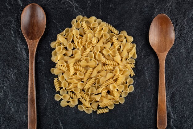 Wooden spoons full of raw farfalle tonde macaroni . 