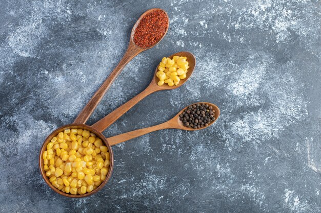 Wooden spoons of ground and grain peppers with bowl of corns.