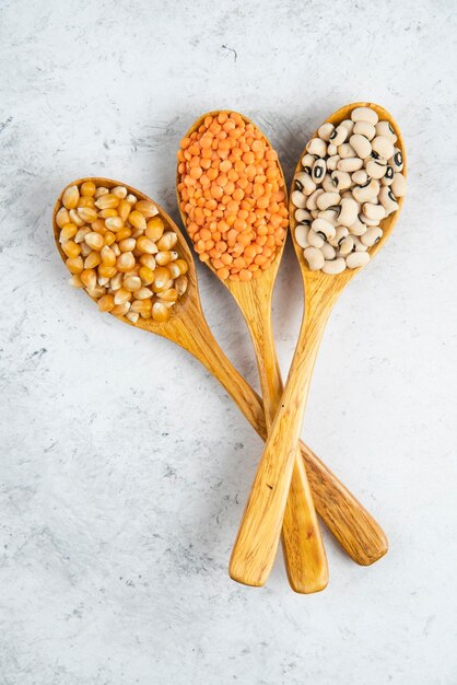 Wooden spoons of various beans and corns on marble surface.