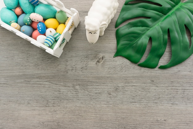 Free photo wooden surface with green leaf, sheep and easter eggs