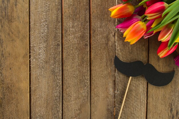 Free photo wooden surface with mustache and colored flowers