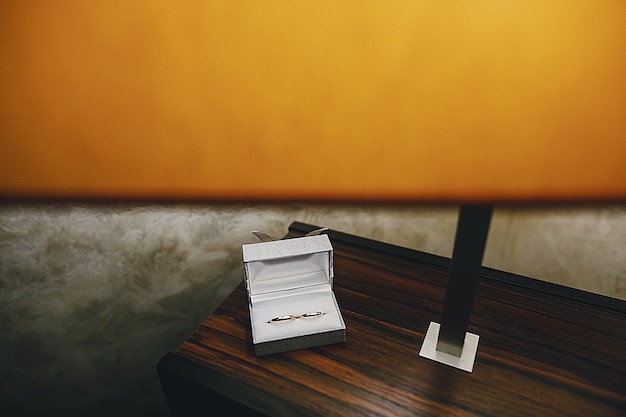 Foto gratuita su un tavolo di legno vicino a una lampada da tavolo c'è una scatola bianca con le fedi