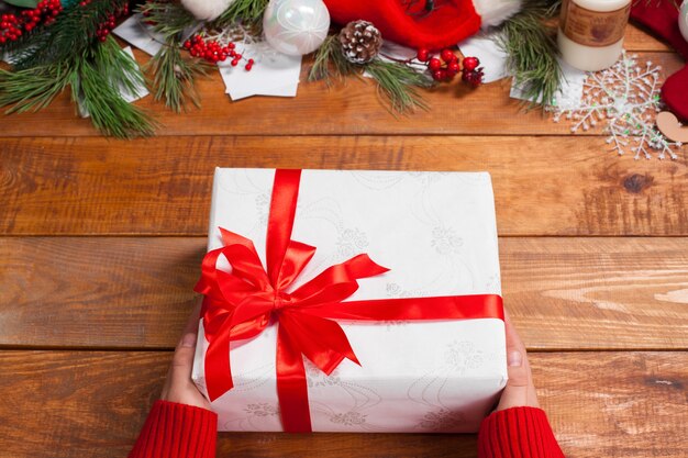 The wooden table with Christmas decorations with hands with gift.