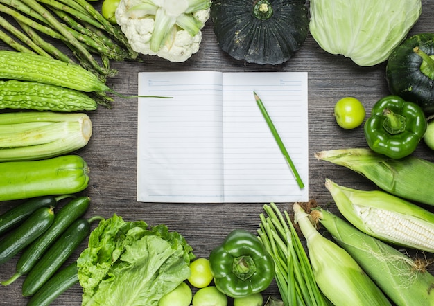 Wooden table with green vegetables and a notebook