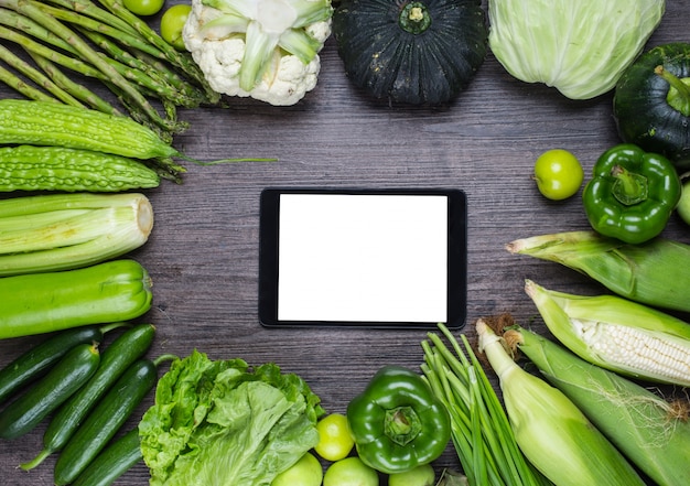 Wooden table with green vegetables and a tablet