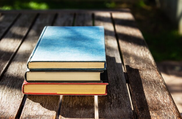 Wooden table with three books on top of each other at daytime