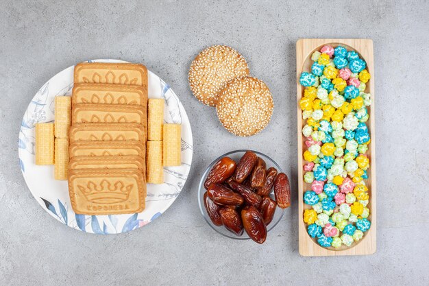 Деревянный поднос с конфетами из попкорна, небольшой порцией фиников, двумя печеньями и бисквитами выстроился на тарелке на мраморном фоне. Фото высокого качества