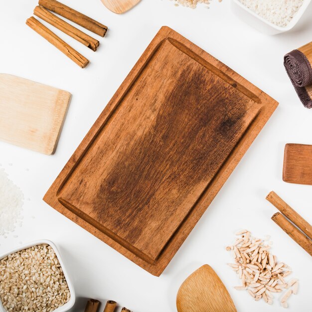 Wooden tray surrounded with uncooked rice; cinnamon sticks; spatula on white background