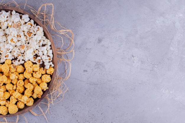 Wooden tray with assortment of popcorn placed on pile of straw on marble background. High quality photo