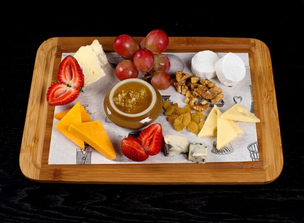 Wooden tray with cheeses, fruits and a jar of honey