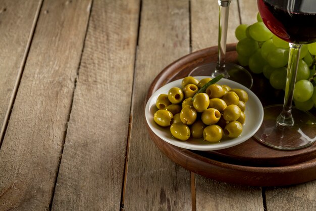 Wooden tray with olives, grapes and wine glasses