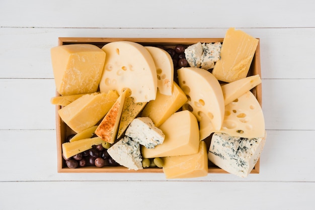 Wooden tray with several slices of the medium-hard swiss cheese with olives green