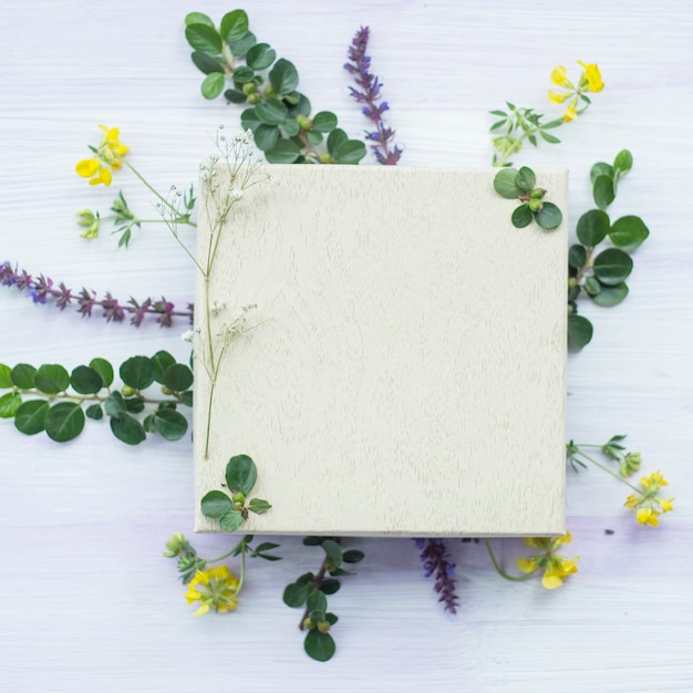 Wooden white blank frame under the flowers and leaves on textured background