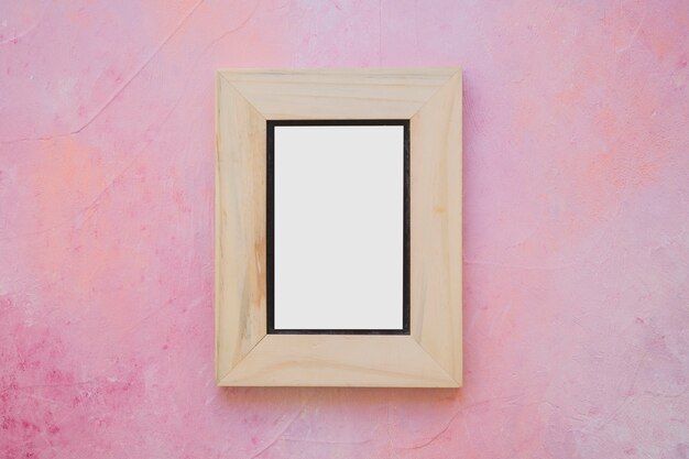 Деревянная рамка с белой рамкой на окрашенной розовой стене