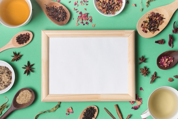 Wooden whiteboard surrounded with different types of herbs on green backdrop