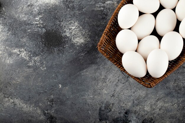 A wooden wicker full of white raw chicken eggs . 