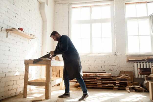 Woodwork and construction. Carpenter using handsaw for sawing wooden plank