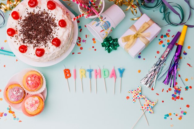 Word birthday candles with party accessories and cake on blue backdrop