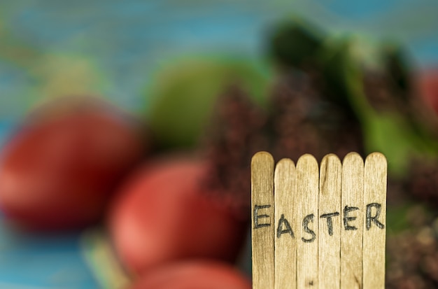 the word Easter in the conceptual block text on wooden sticks, beautiful festive eggs with greens