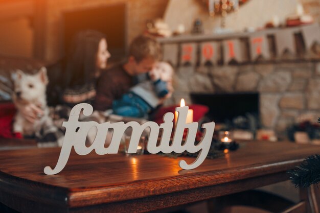 Word "family" with a family sitting on the sofa in the background on christmas