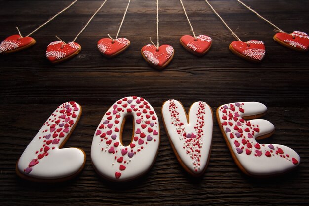 Word "love" made of cookies with heart-shaped cookies hanging from ropes on a wooden table