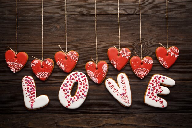 Word "love" made of cookies with heart-shaped cookies hanging from ropes on a wooden table