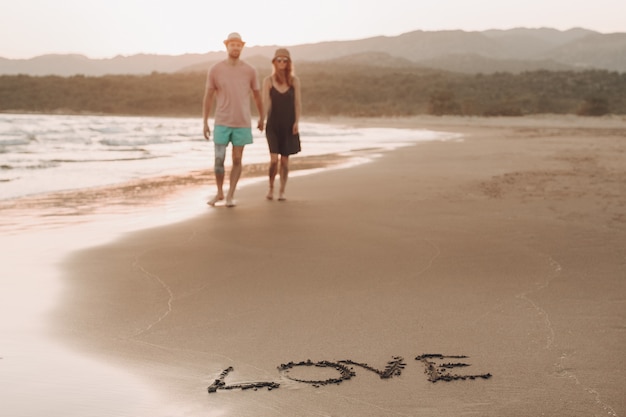слово Любовь на побережье песка и размытые любви пара на фоне ходьбы