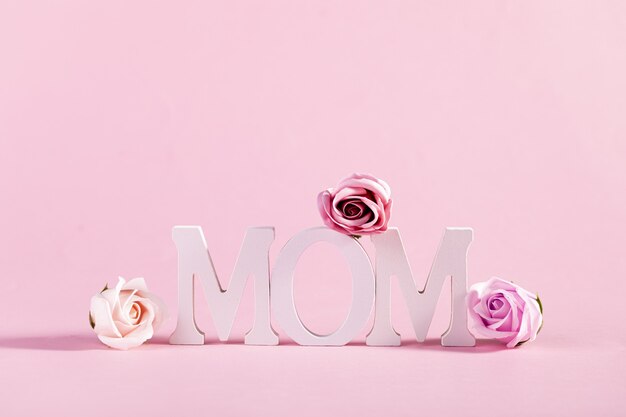 Word "Mom" decorated with flowers on pastel pink background