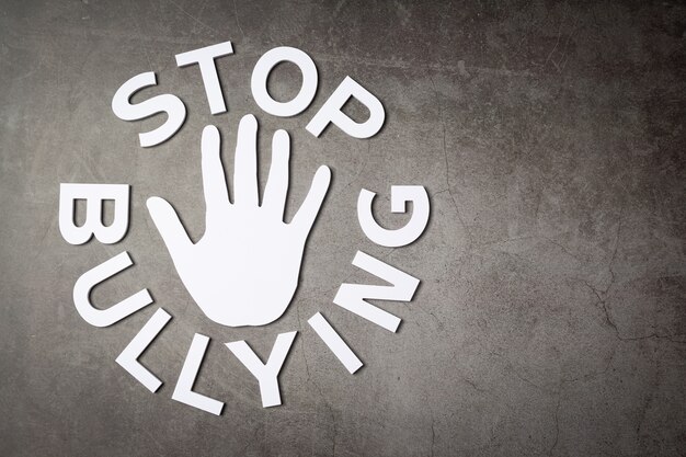 Word "stop bullying" with hand sign on dark wall