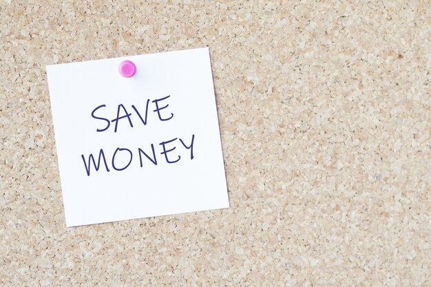 Words "save money" on a paper attached to a board with a pin